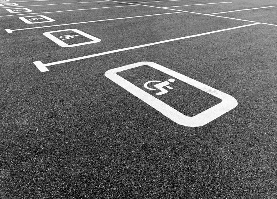 Close-up of a designated disabled parking space on an asphalt surface, featuring a worn yellow wheelchair symbol painted on the ground. Surrounding the symbol, the asphalt displays a textured dark gre