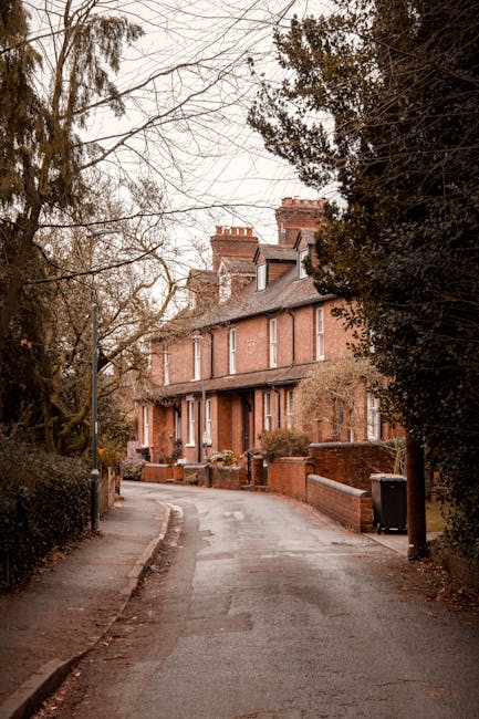 A wide view of a residential street with white Victorian-style terraced houses on both sides, showcasing detailed architectural facades and wrought iron balconies. The street features a mix of parked 